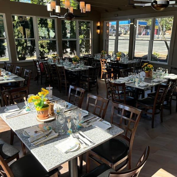 Ancona Bistro's dining room with set tables, dark chairs, and large windows overlooking a street.