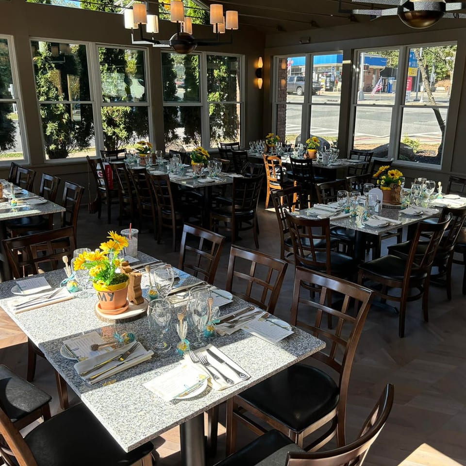 Ancona Bistro's dining room with set tables, dark chairs, and large windows overlooking a street.