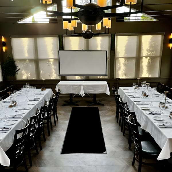 Ancona Bistro's private dining room with two long tables set for guests and a projection screen.