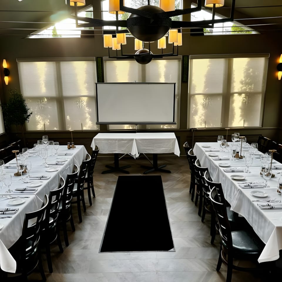 Ancona Bistro's private dining room with two long tables set for guests and a projection screen.