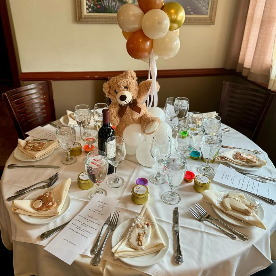 A set table at Ancona Bistro with a teddy bear, balloons, wine, and place settings with menus.