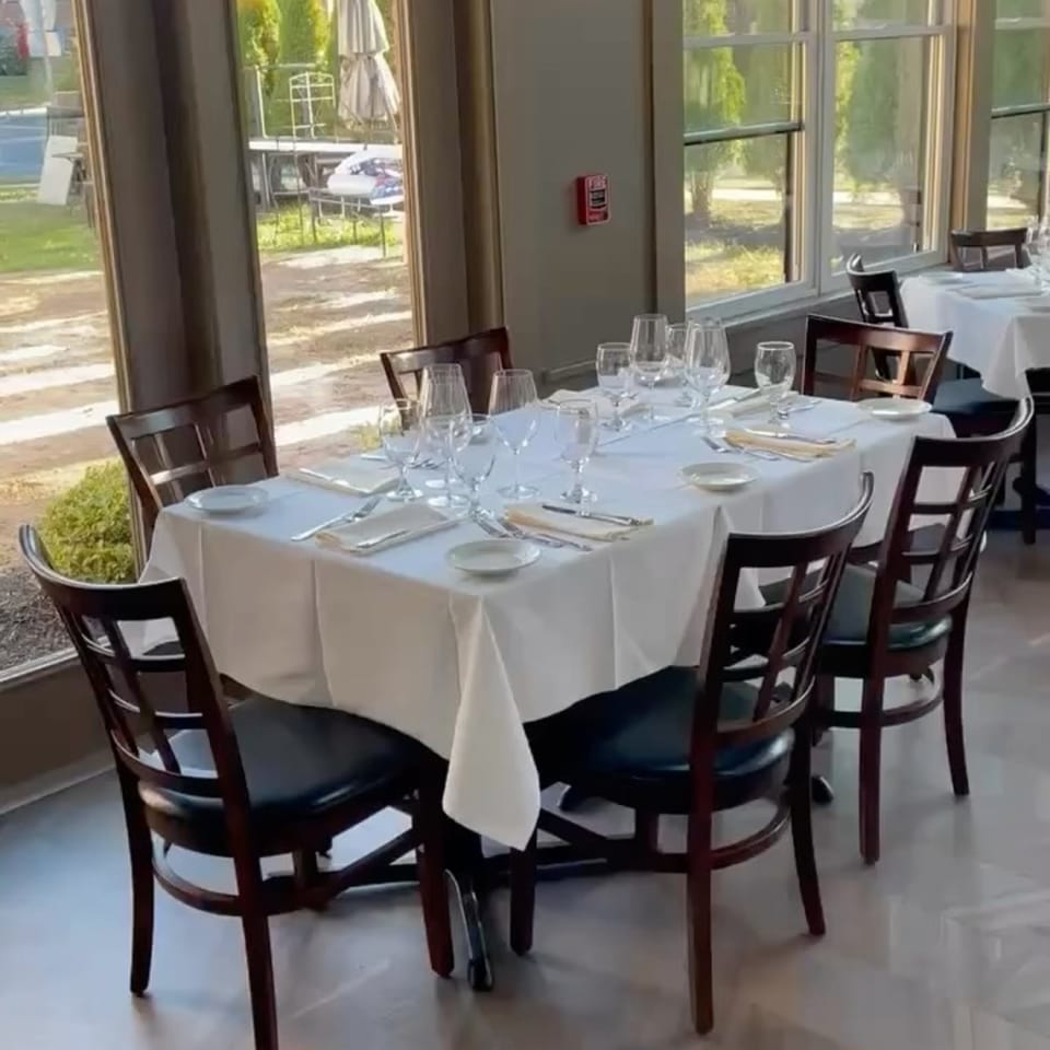 Ancona Bistro dining room with a long table set for six, featuring white tablecloths and dark chairs.